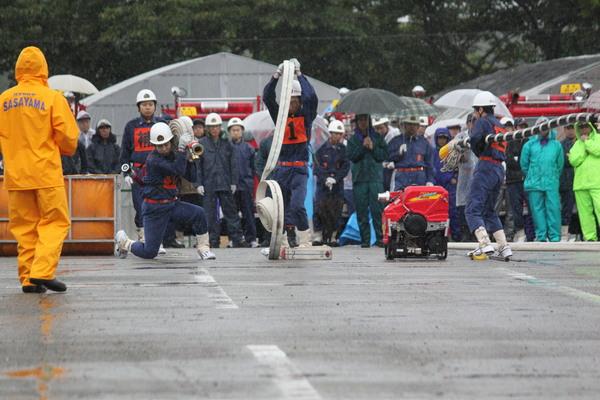 雨の中、篠山市消防団の3名が、ホースを運んだり、丸くまかれたホースを一気に伸ばしている写真